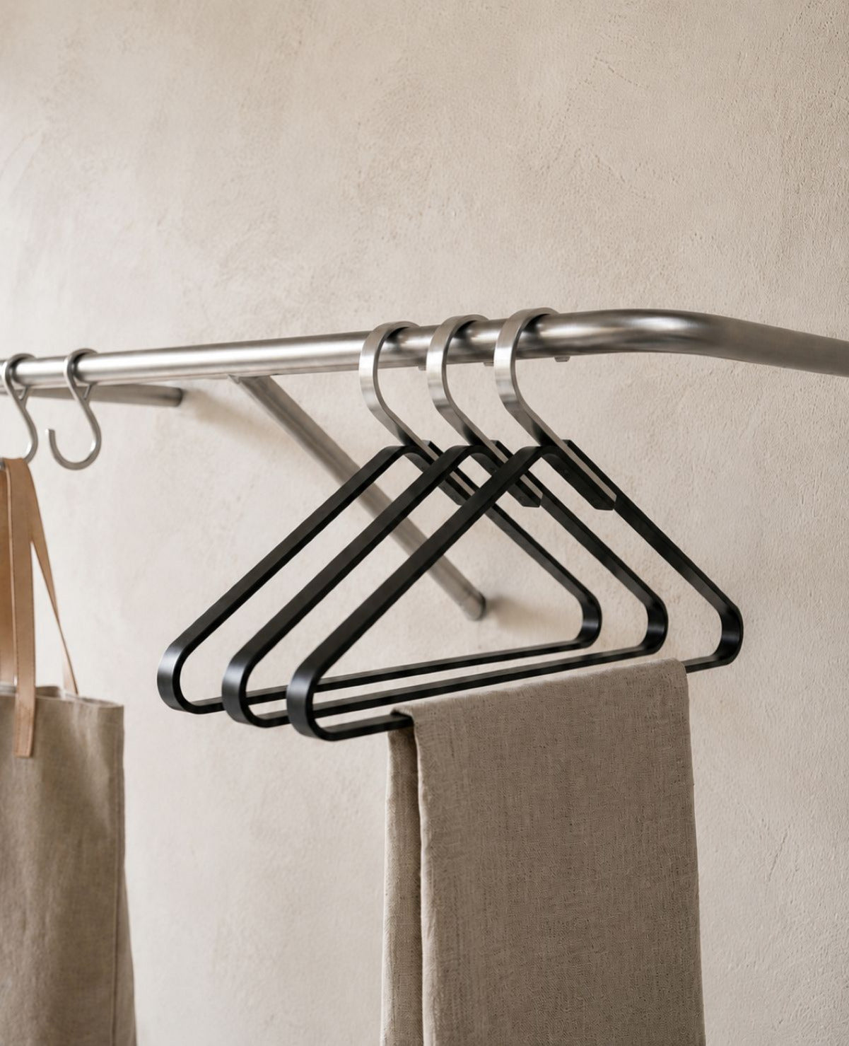 Schwarze Design-Kleiderbügel aus Metall an einer Edelstahl-Garderobe in modernem, hellem Eingangsbereich von Siqual Design.
