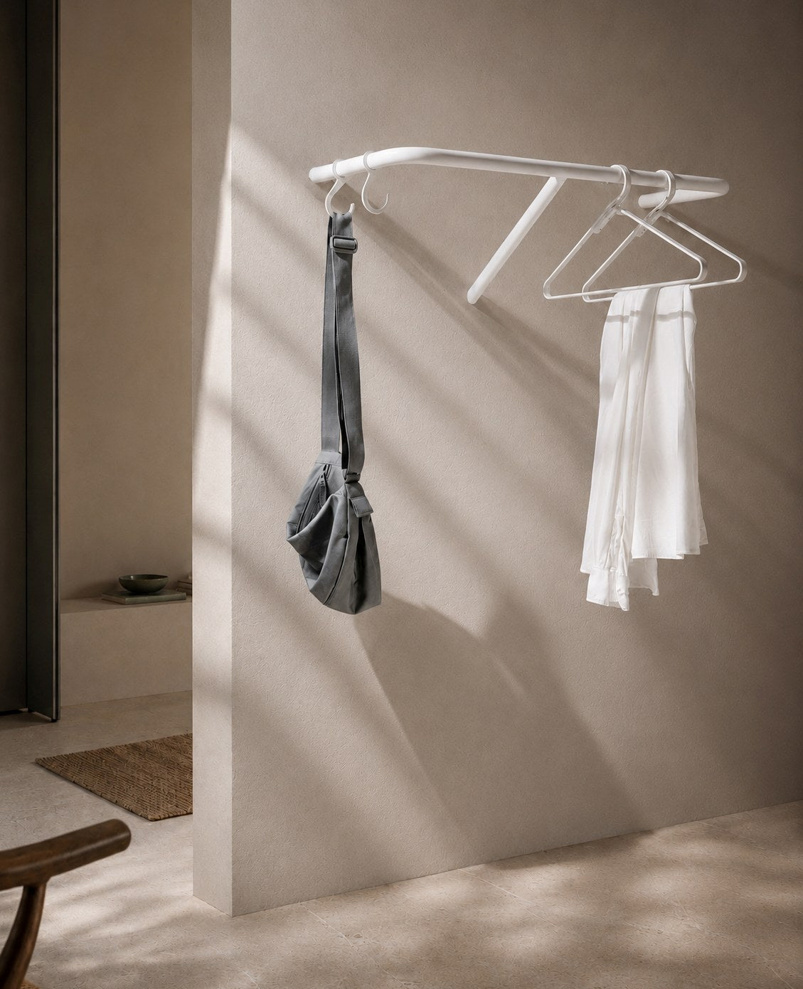 Weiße Wandgarderobe aus Metall mit Bügeln, Tasche und Shirt in einem modernen, hellen Eingangsbereich von Siqual Design.