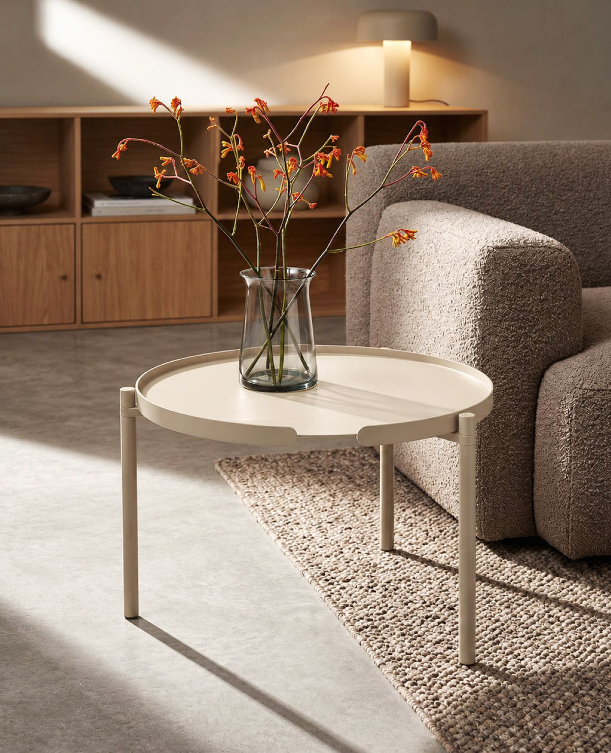 Runder Couchtisch aus Metall in Champagnerbeige von Siqual Design, mit Glasvase und Zweigen, neben einem grauen Sofa im modernen Wohnzimmer.