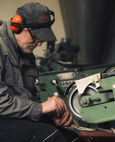 Mitarbeiter in einer europäischen Metallmanufaktur beim Schleifen eines Metallteils – handwerkliche Fertigung und Metallverarbeitung für Siqual Design.