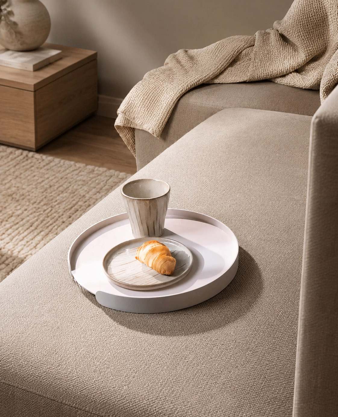 Weißes rundes Metalltablett Milo von Siqual Design auf hellem Stoffsofa mit Kaffeebecher, Keramikteller und Croissant in moderner Wohnszene.
