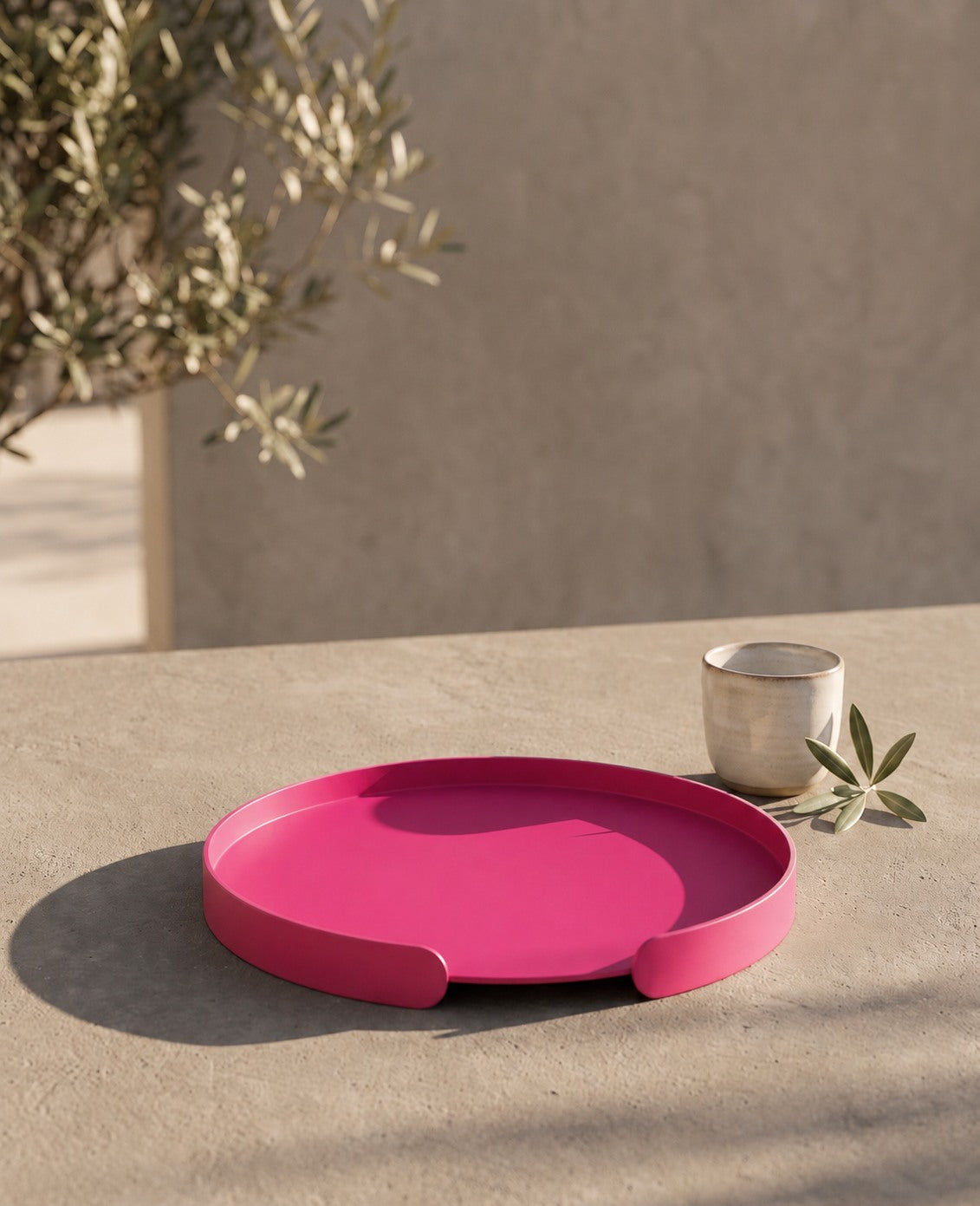 Magenta Serviertablett aus Metall von Siqual Design auf hellem Steintisch mit Keramikschale und Olivenzweig in moderner mediterraner Szene.