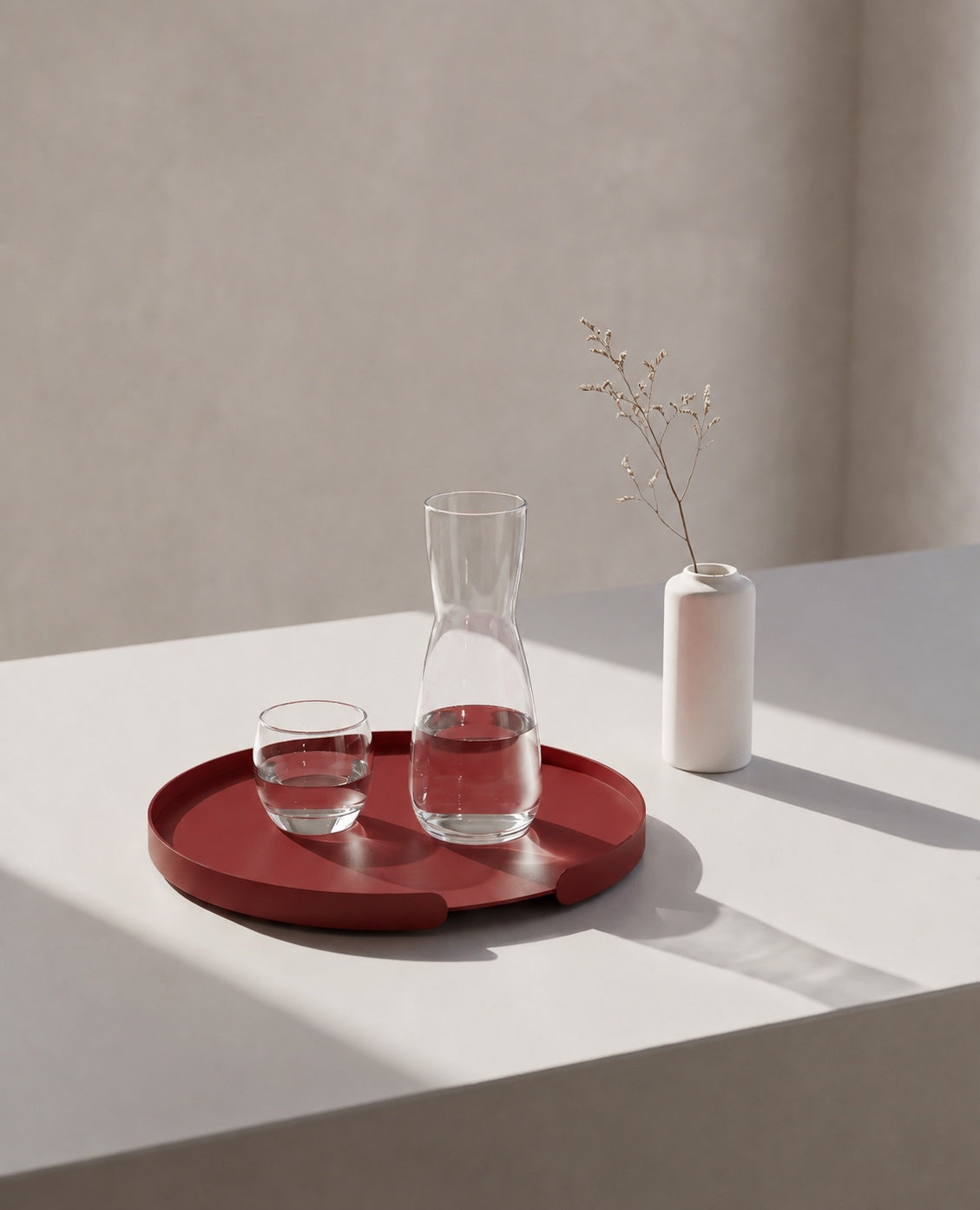 Rundes Tablett aus Metall in Purpurrot von Siqual Design mit Glas und Wasserkaraffe, dekorativ auf einem hellen Untergrund arrangiert.