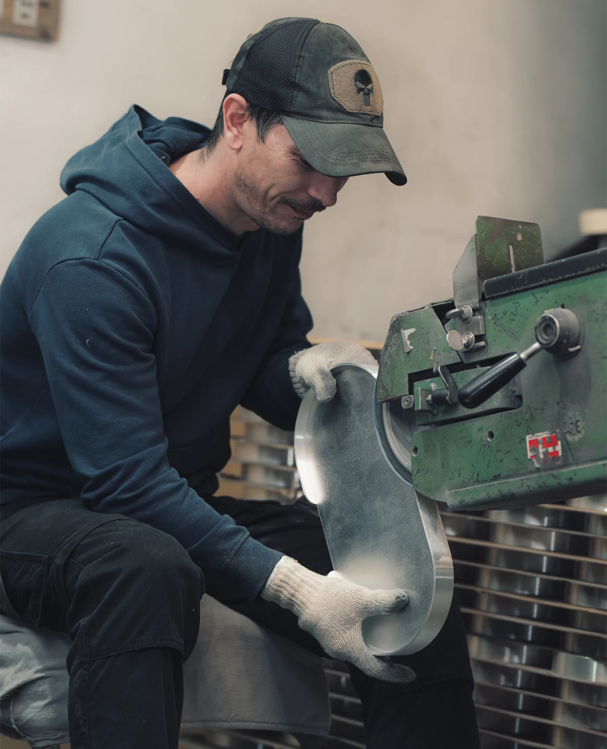 Mitarbeiter schleift ein Metalltablett an der Schleifmaschine in der Siqual Design Manufaktur