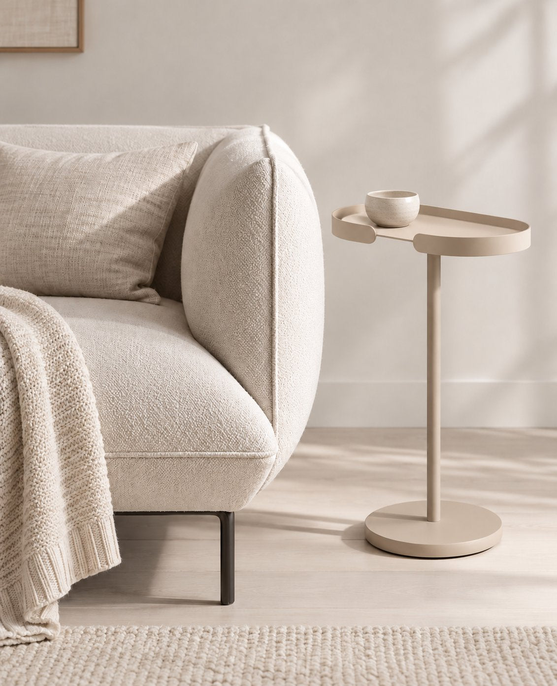 STAN Beistelltisch aus Metall in Champagne Beige neben einem beigen Sofa, mit Keramikschale auf der ovalen Tischplatte.