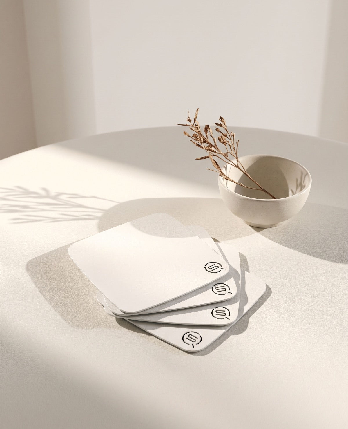 PLAZA Design-Untersetzer aus Edelstahl in Weiß von Siqual Design als hochwertiges 4er-Set auf modernem Tisch mit minimalistischer Dekoration.