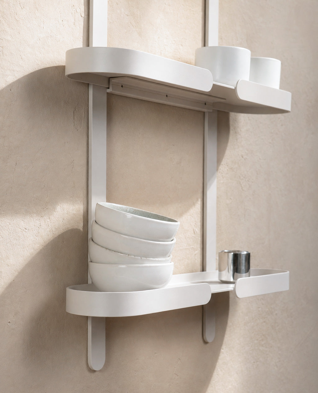 Detailaufnahme eines weißen Siqual Design Wandregals aus Metall mit Keramikschalen und Tassen auf warmer, strukturierter Küchenwand.
